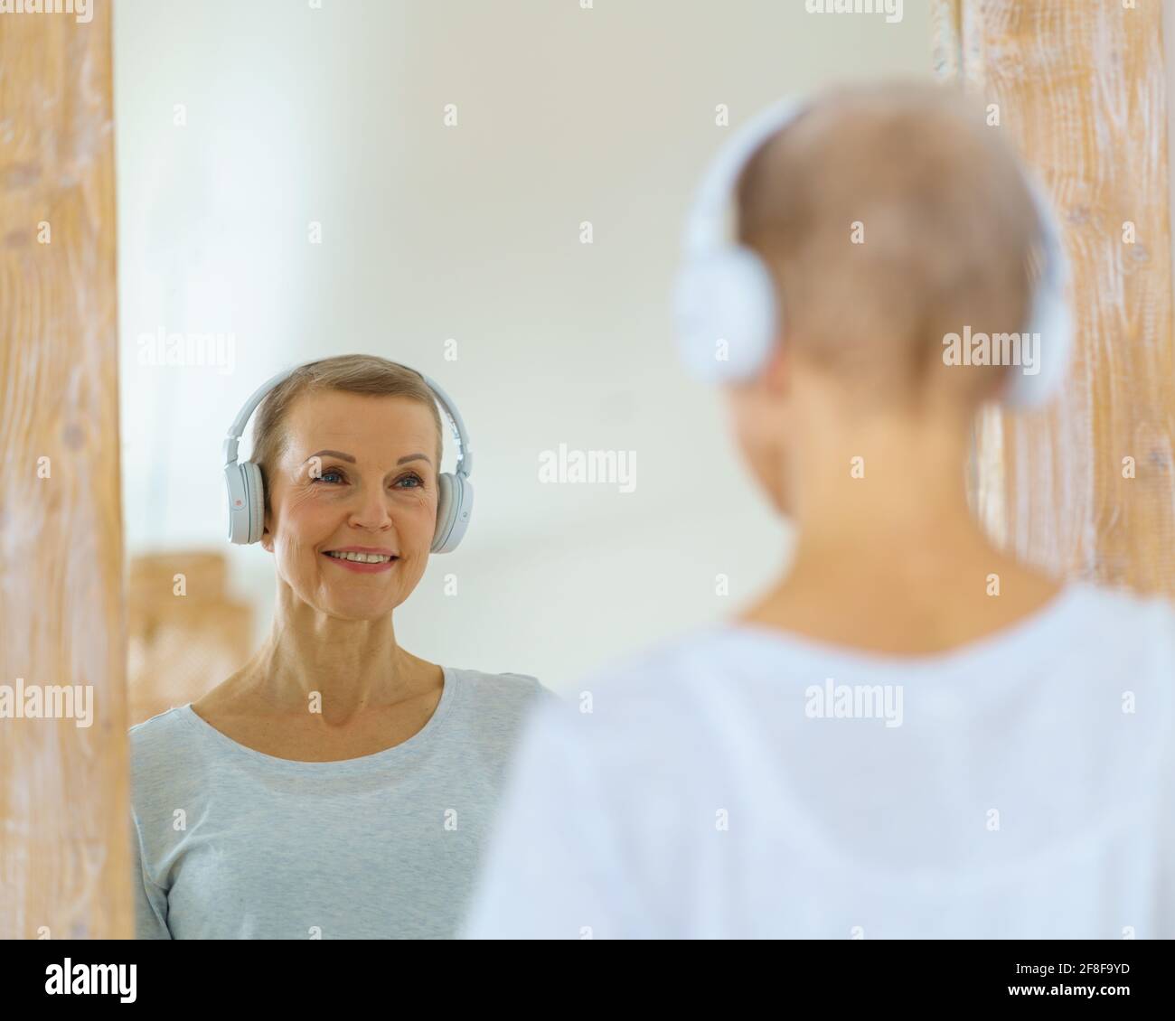 Donna anziana dai capelli grigi che si ammira nello specchio. La donna di mezza età si guarda. Mature bella donna bionda con i capelli di colpo admires riflessione in piedi davanti al grande specchio Foto Stock