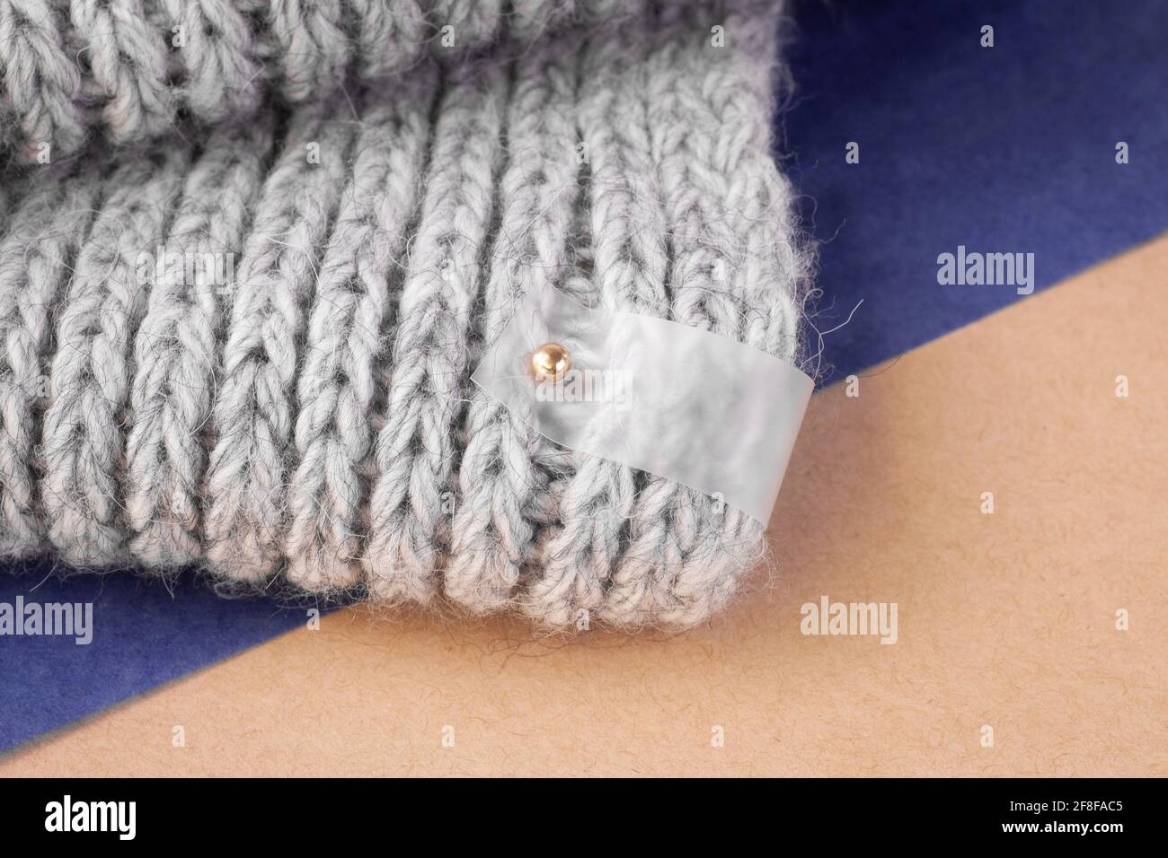 etichetta trasparente in bianco opaco macro per logo su sciarpa grigia a maglia su sfondo moderno sigillato di carta velina blu e beige artigianale Foto Stock