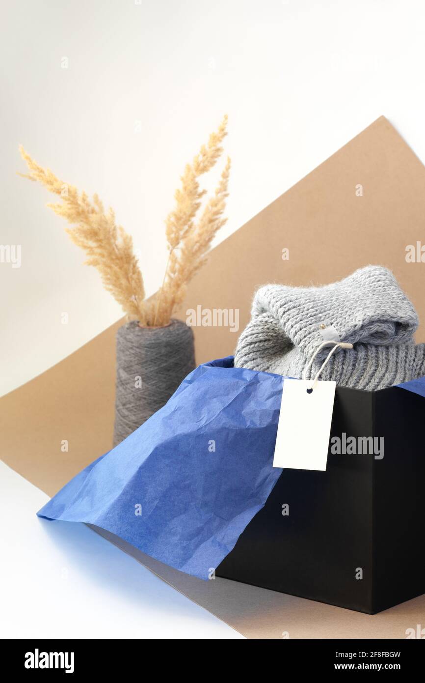 etichetta o etichetta bianca di carta bianca per il marchio su sciarpa grigia in maglia in scatola nera e blu carta tissue ed erba di pampas essiccata in un filato di bobina vaso Foto Stock