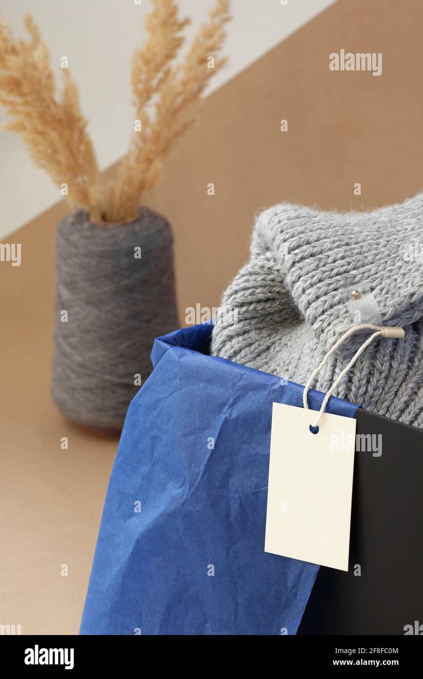 etichetta con logo in carta bianca bianca macro su una maglia grigia sciarpa in una scatola nera e pampas asciugato erba in un vaso di filato di bobina su carta beige Foto Stock