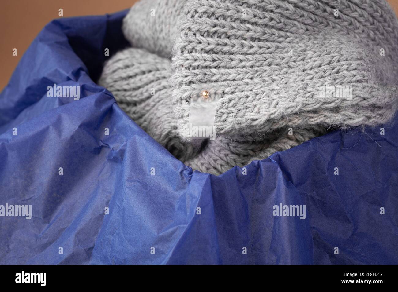 tag trasparente opaco macro su sciarpa grigia in maglia una scatola nera confezionata con carta di tessuto blu Foto Stock