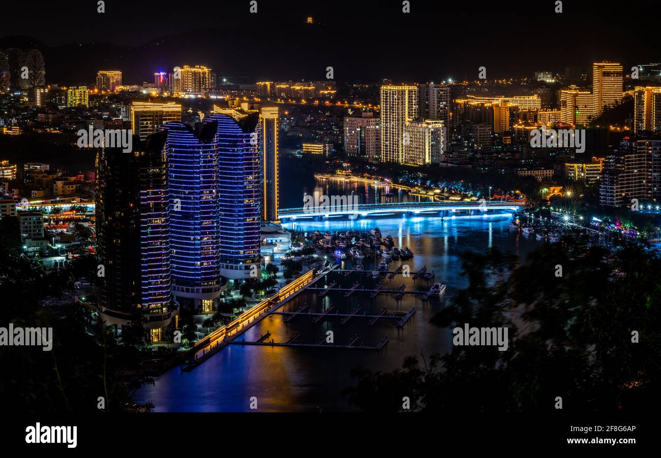 Panorama panoramico della città di Sanya illuminata di notte con Sanya Ponte sul fiume e edifici moderni nell'isola di Sanya Hainan, Cina Foto Stock