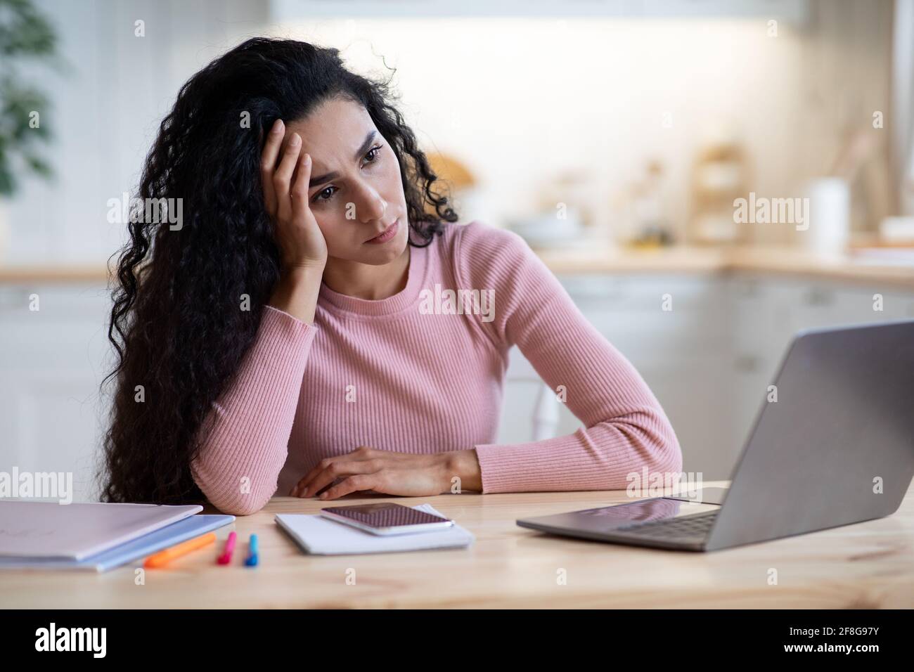 Crisi della creatività. Donna sconvolto seduta alla scrivania con computer portatile in cucina interno Foto Stock