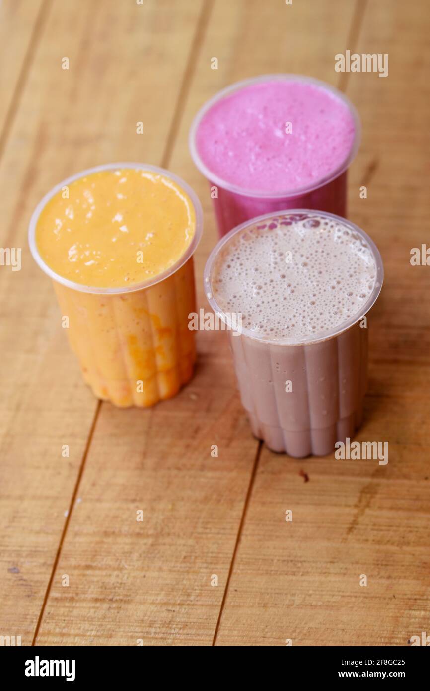Tre bicchieri di vari milkshakes fragola, cioccolato e vaniglia frullato su sfondo di legno Foto Stock