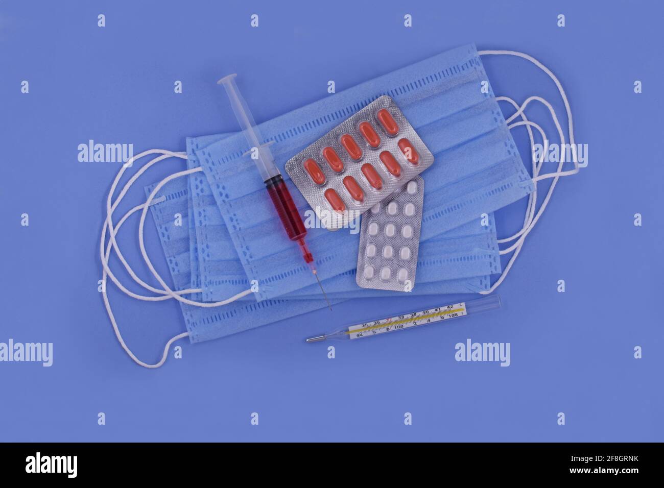 Maschera medica protettiva, pillole, termometro, siringa su sfondo blu, protezione da virus corona, coronavirus, covid19 pandemia globale Foto Stock