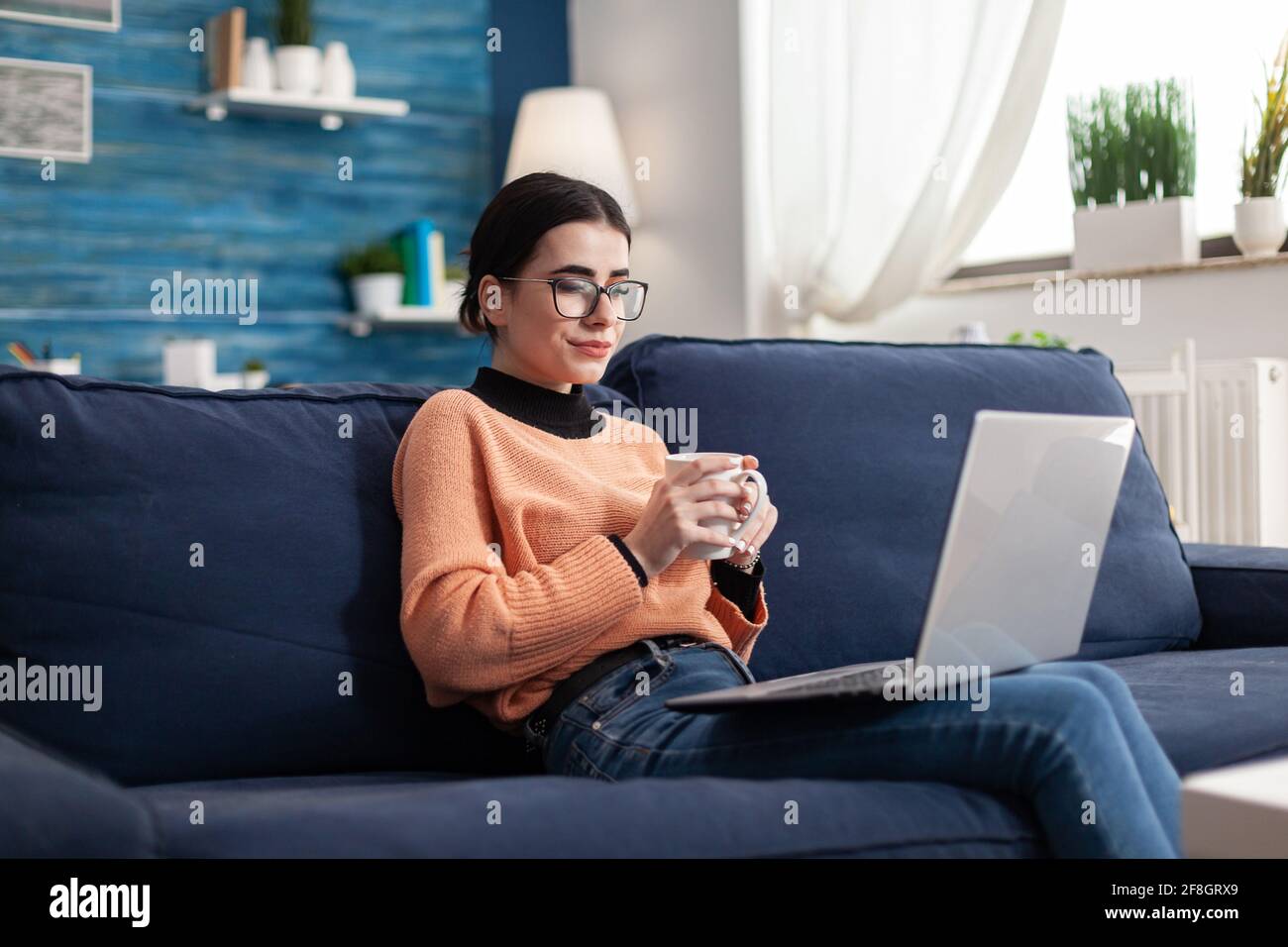 Corso online di gestione dell'apprendimento dell'università degli studenti durante il seminario di univeristy. Giovane donna seduta sul divano in soggiorno che controlla la piattaforma di e-learning usando un computer portatile Foto Stock