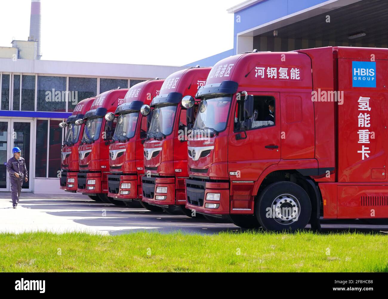 (210414) -- TANGSHAN, 14 aprile 2021 (Xinhua) -- UN operaio passa accanto a cinque camion pesanti alimentati a idrogeno di recente introduzione nella zona di sviluppo economico di Tangshan Haigang, provincia di Hebei, 14 aprile 2021. Mercoledì, la Tangshan Haigang Economic Development zone ha introdotto cinque veicoli pesanti alimentati a idrogeno. La flotta di autocarri è tra i primi tentativi della zona di ottimizzare la struttura industriale e il consumo energetico sostituendo gradualmente il carburante diesel con le celle a idrogeno più ecocompatibili. (Xinhua/Yang Shiyao) Foto Stock