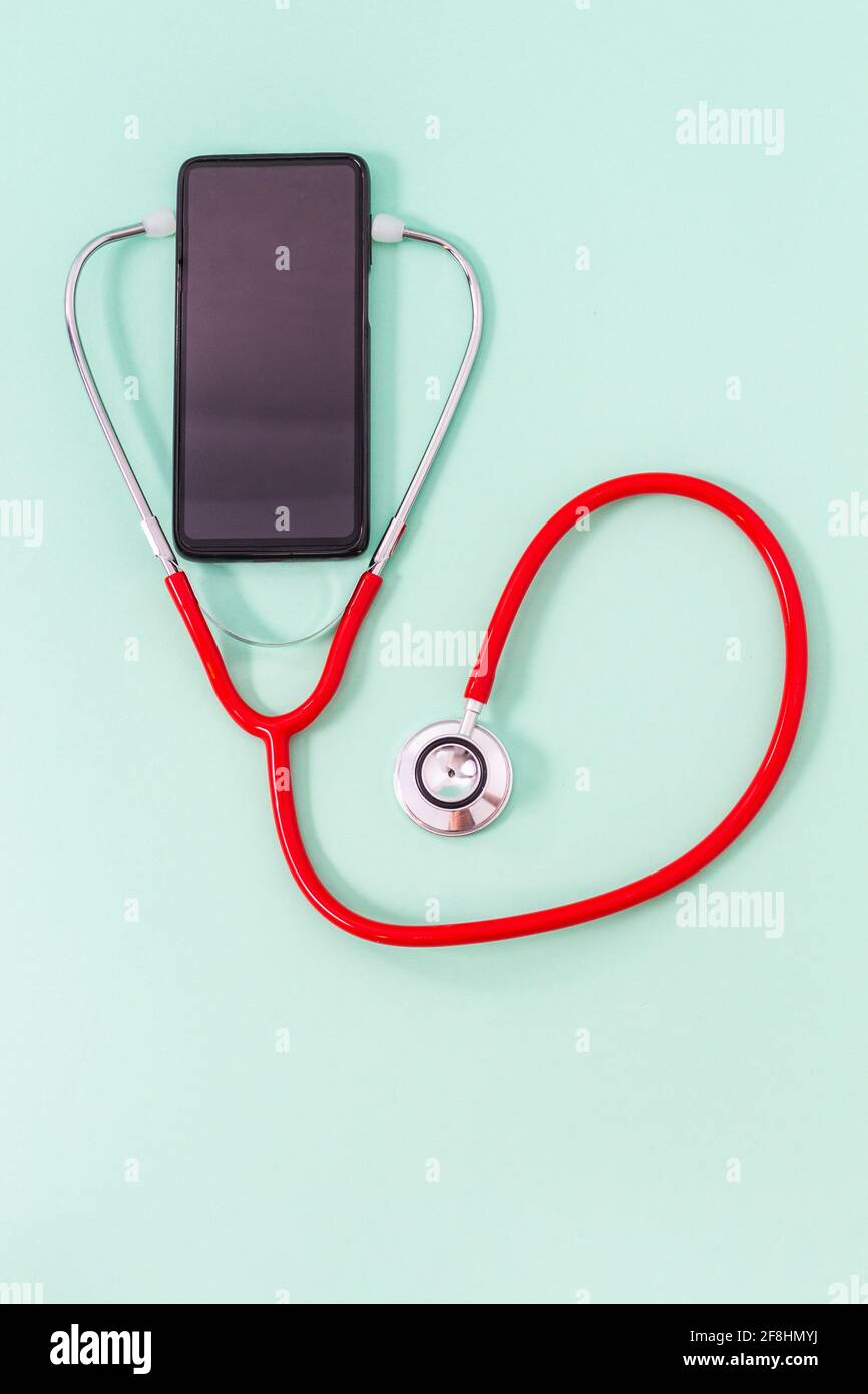 Vista dall'alto di uno stetoscopio rosso con cuffia con stetoscopio rosso su sfondo verde. Concetto medico e di comunicazione o riparazione di telefoni cellulari. Foto Stock