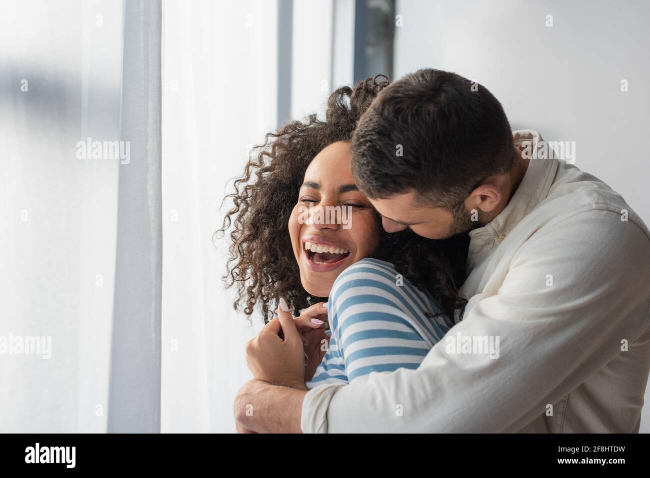allegra coppia multietnica abbracciata a casa Foto Stock