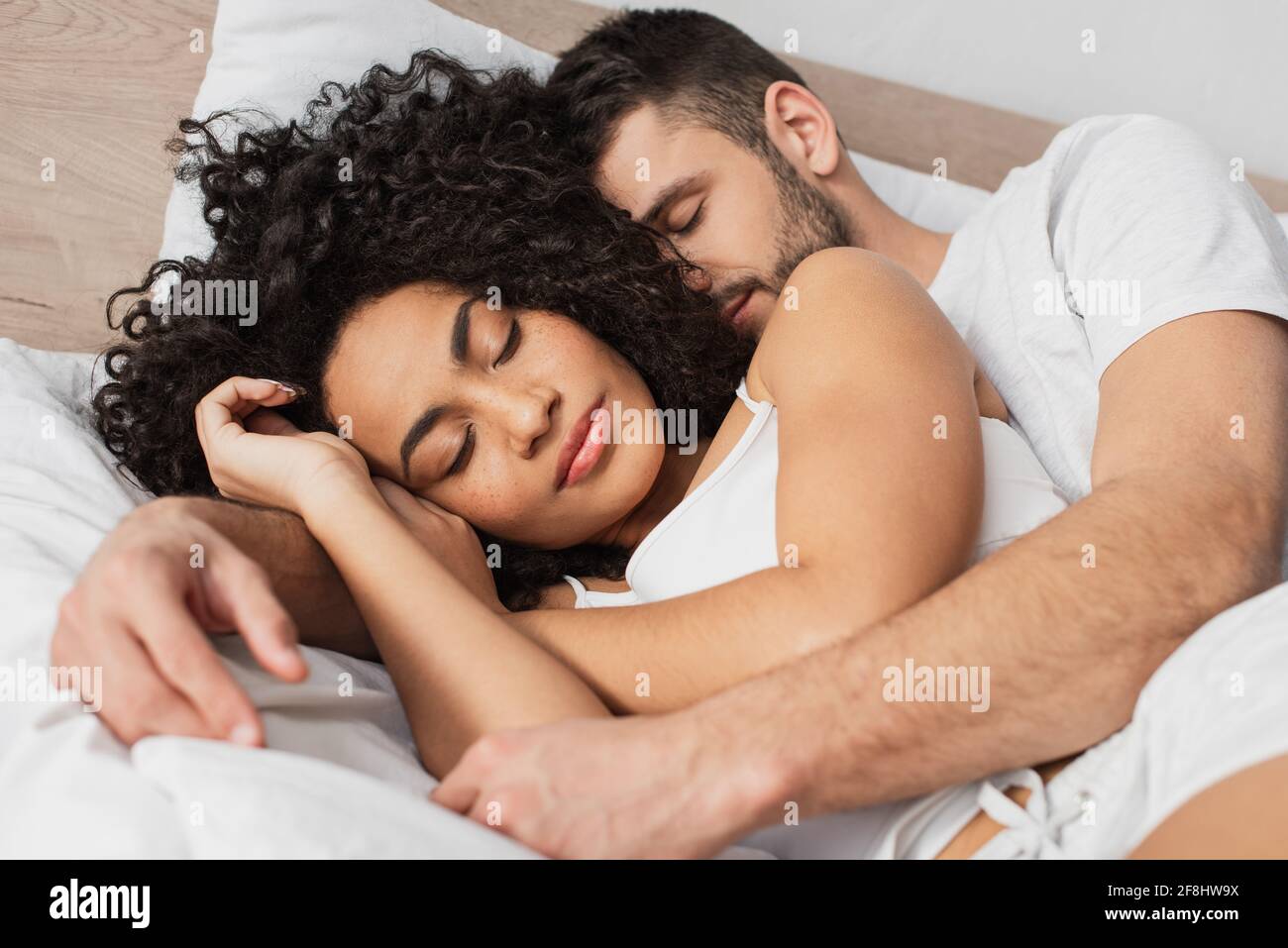 uomo multietnico e donna che abbracciano mentre dormono a letto Foto Stock