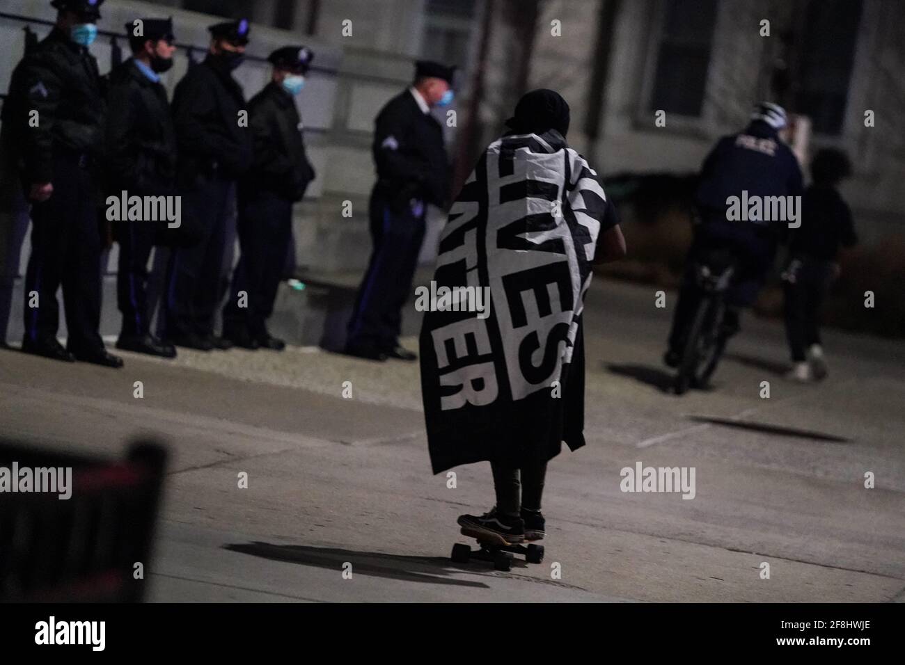 Philadelphia, Stati Uniti. 13 Apr 2021. Un dimostratore che indossa una bandiera Black Lives Matter fa una skateboard di fronte agli ufficiali della polizia di Philadelphia durante una protesta di Justice for Daunte Wright a Philadelphia, USA. Daunte Wright era un uomo nero di 20 anni che fu ucciso e ucciso da un agente di polizia a Brooklyn Center, Minnesota, il 11 aprile. Credit: Chase Sutton/Alamy Live News Foto Stock