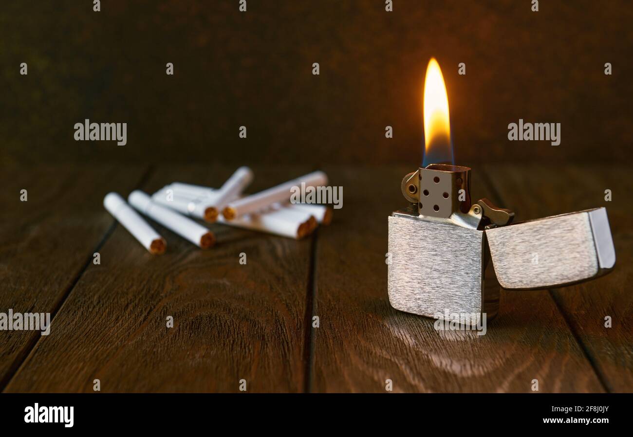 Accendino in metallo d'epoca con fiamma e sigarette su sfondo scuro, primo piano Foto Stock