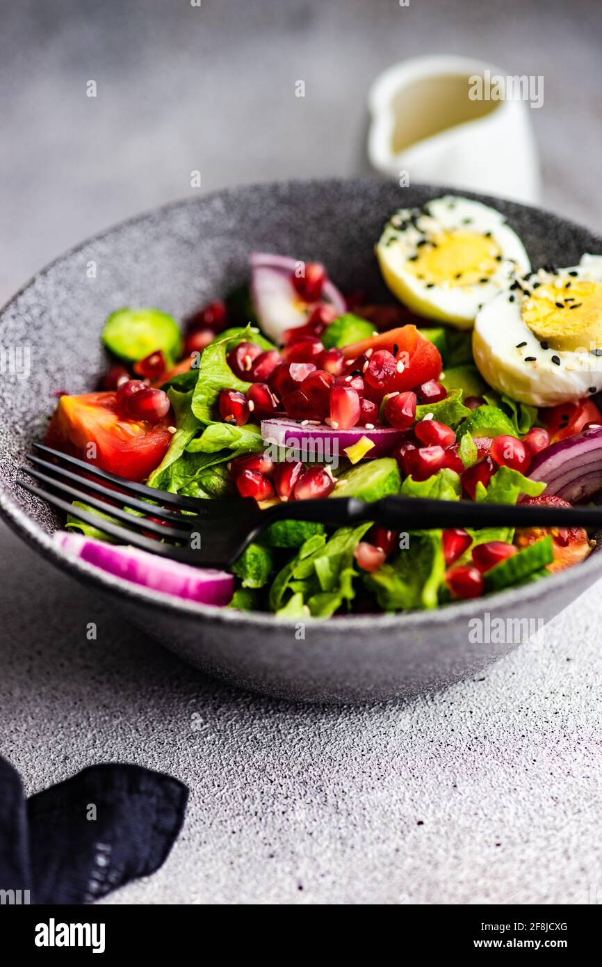 Insalata con lattuga, pomodoro, cipolla rossa, semi di melograno e un uovo bollito con semi di sesamo Foto Stock