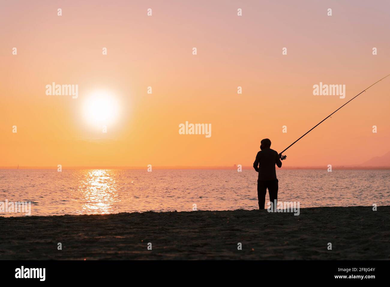 Silhouette di uomo in pesca onde sulla spiaggia al tramonto Foto Stock