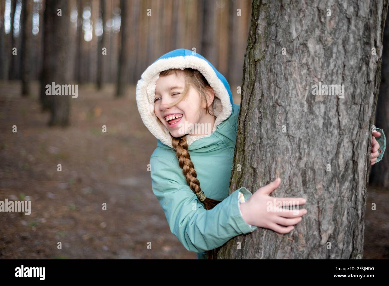 Ragazza teen che guarda fuori da dietro l'albero nel foresta e ridere Foto Stock
