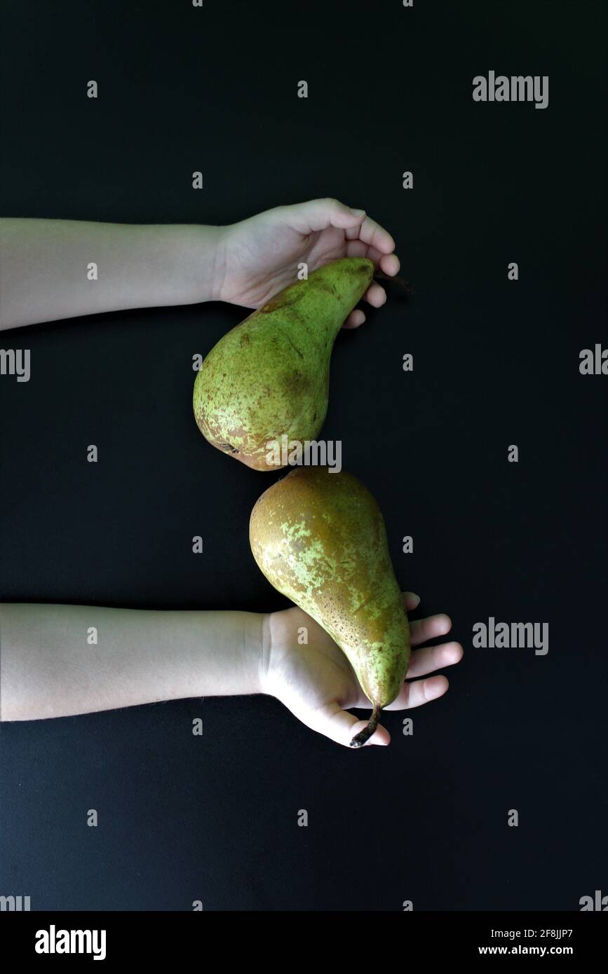 Su uno sfondo nero, due mani tengono due pere Foto Stock