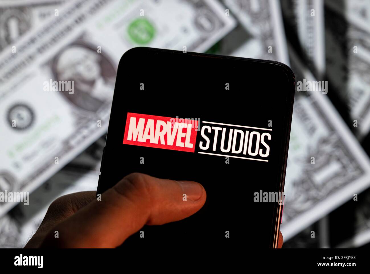 In questa illustrazione fotografica, l'etichetta americana di produzione di film di proprietà di Disney, Marvel Studios, il logo è visto su uno schermo di un dispositivo mobile Android con la valuta dell'icona del dollaro degli Stati Uniti, simbolo dell'icona in dollari sullo sfondo. Foto Stock