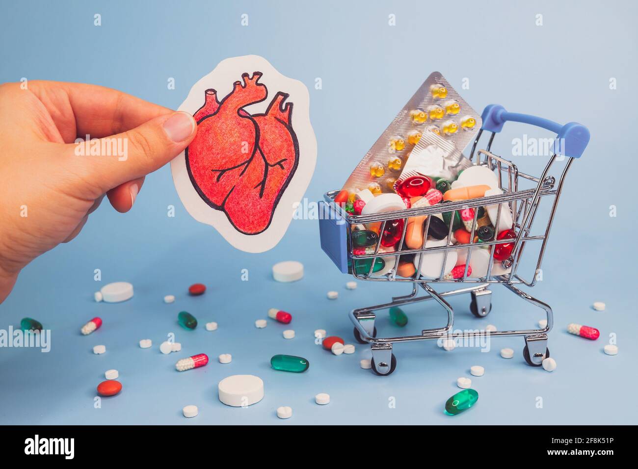 Trattamento o prevenzione di malattie cardiache con varietà di pillole. Matita di cuore umano in mano contro sfondo di molte pillole colorate in groce Foto Stock