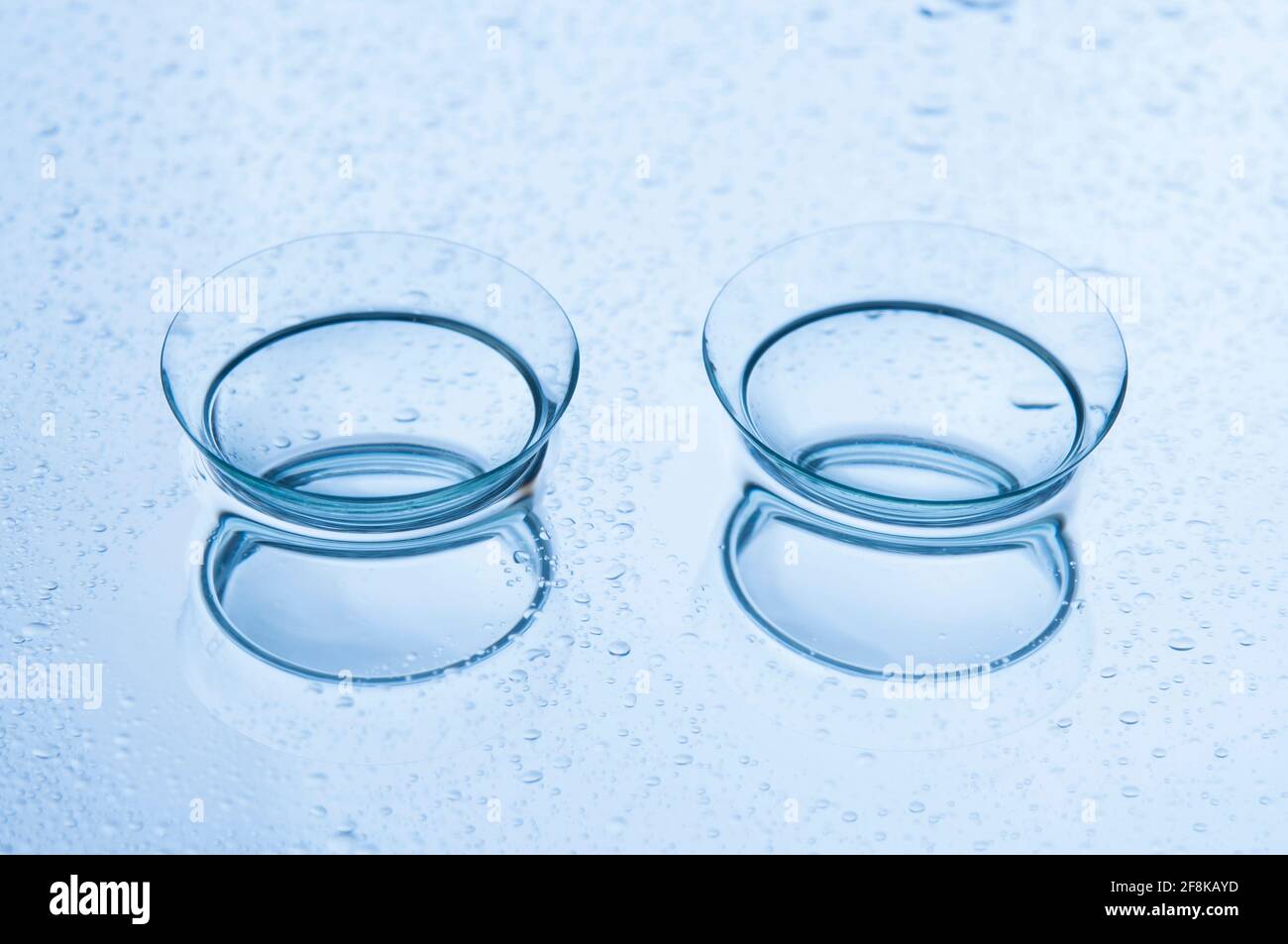 Primo piano di due lenti a contatto morbide con riflessi su sfondo azzurro con gocce. Foto Stock