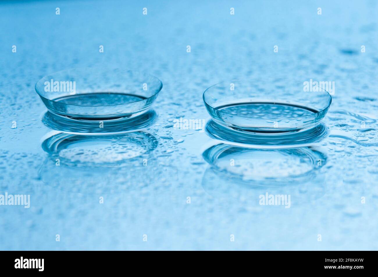 Primo piano di due lenti a contatto morbide con riflessi su sfondo azzurro con gocce. DOF poco profondo. Foto Stock