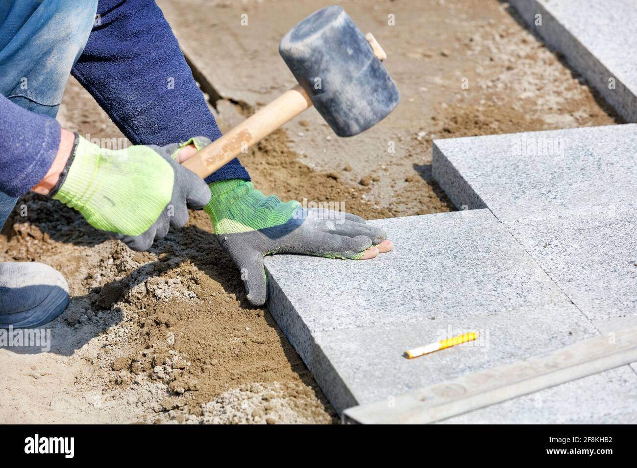Un lavoratore depone blocchi di granito sul marciapiede con un martello di gomma. Foto Stock
