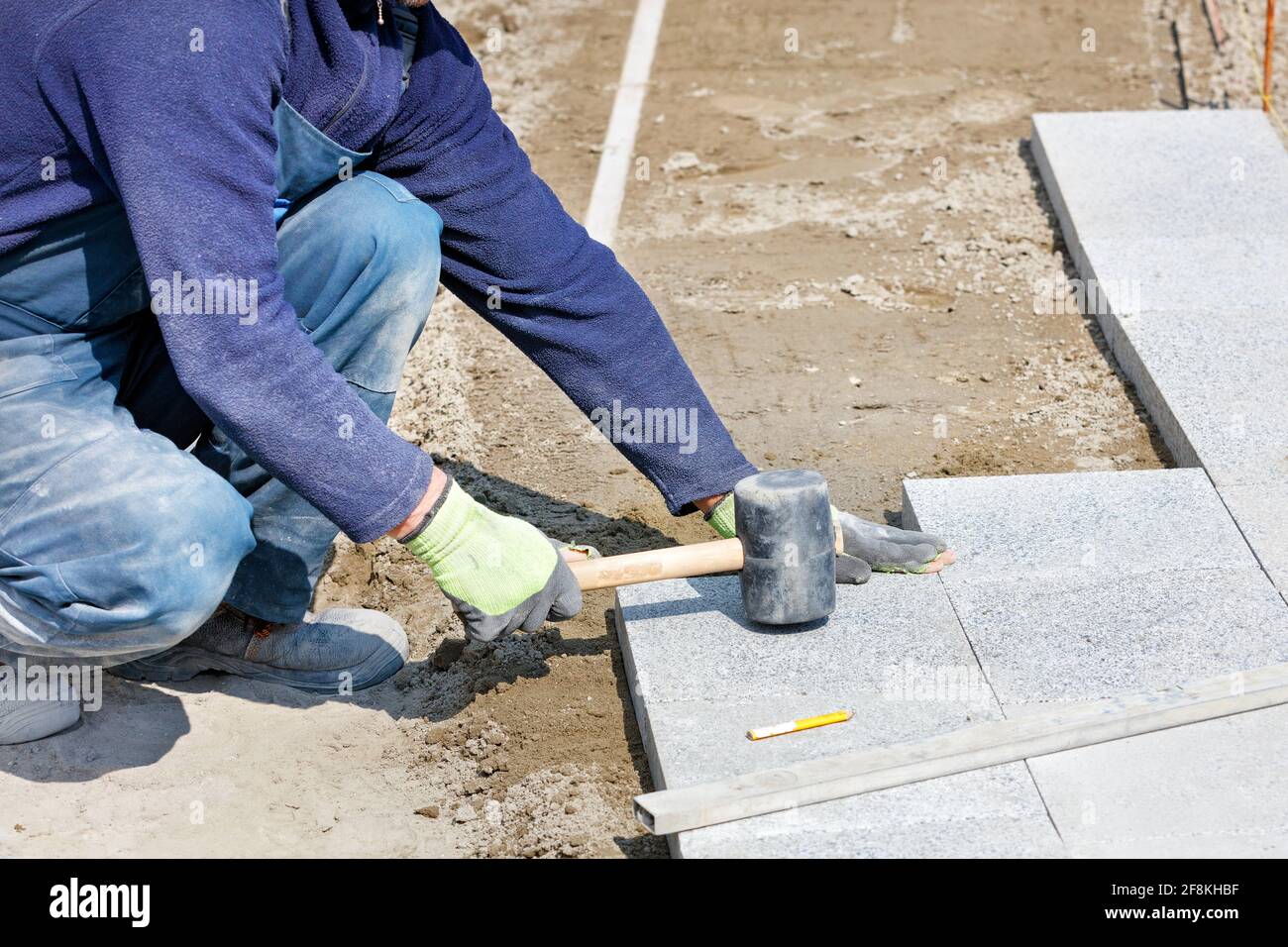 Un lavoratore dispone blocchi di granito sul marciapiede con un martello di gomma su un'area contrassegnata. Foto Stock