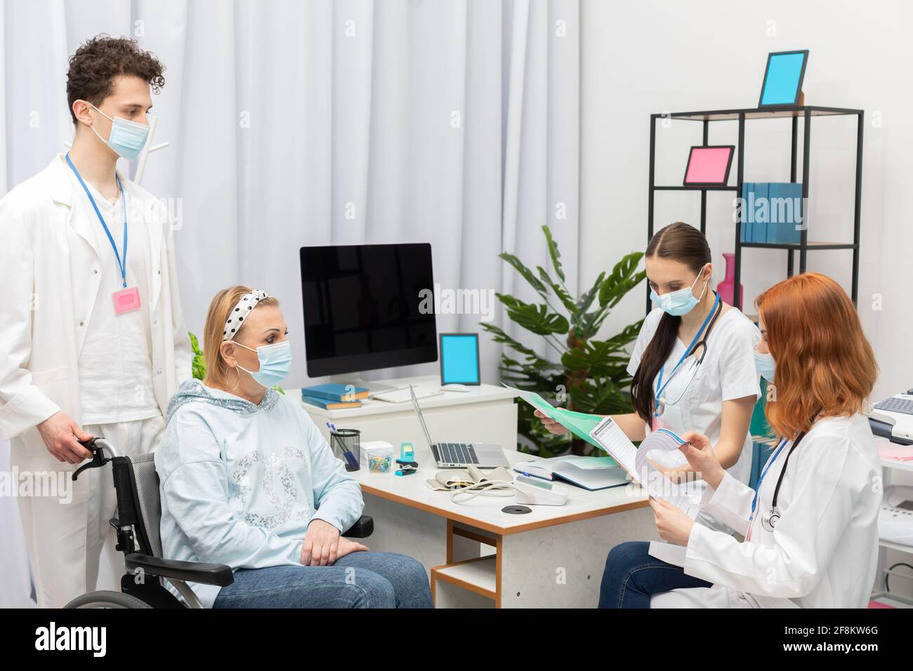 Prima della visita, il medico controlla attentamente l'anamnesi del paziente per eventuali pandemie. Una donna di 50 anni in sedia a rotelle nell'ufficio del medico. Foto Stock