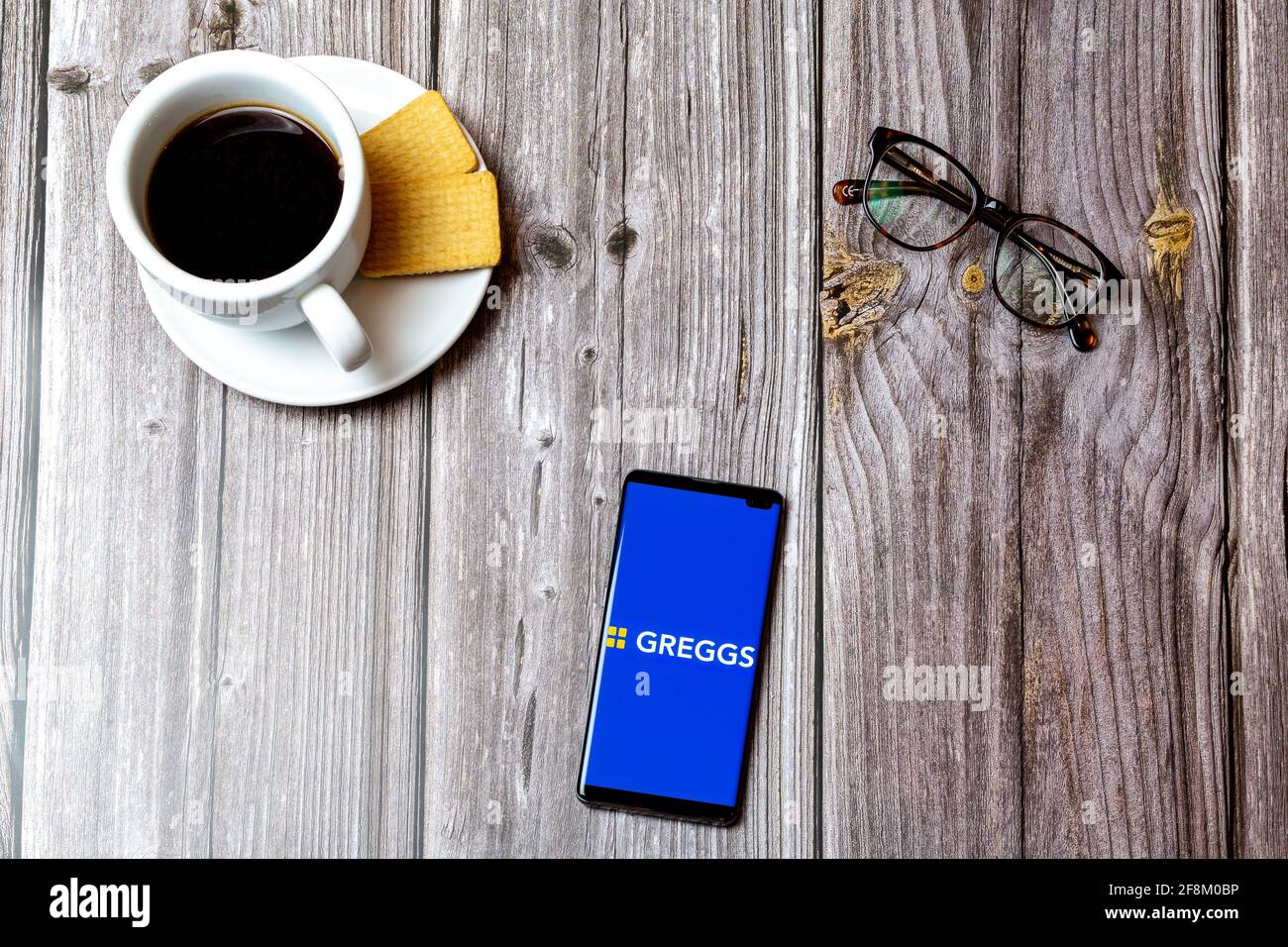 Un telefono cellulare o un telefono cellulare posato su un legno Tabella che mostra l'applicazione Greggs sullo schermo Foto Stock