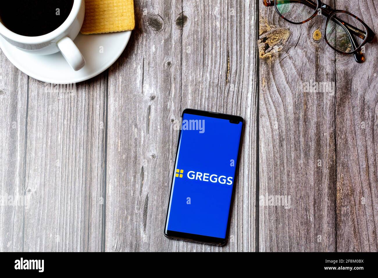 Un telefono cellulare o un telefono cellulare posato su un legno Tabella che mostra l'applicazione Greggs sullo schermo Foto Stock