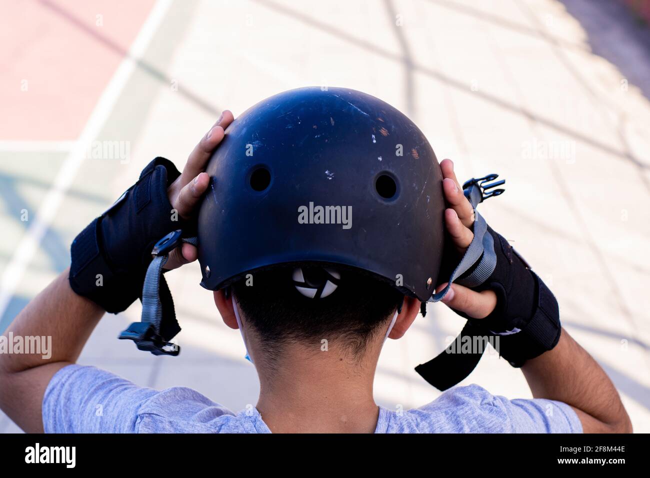 Primo piano da dietro di un pretesto che indossa il casco, preparandosi a pattinare. Foto Stock