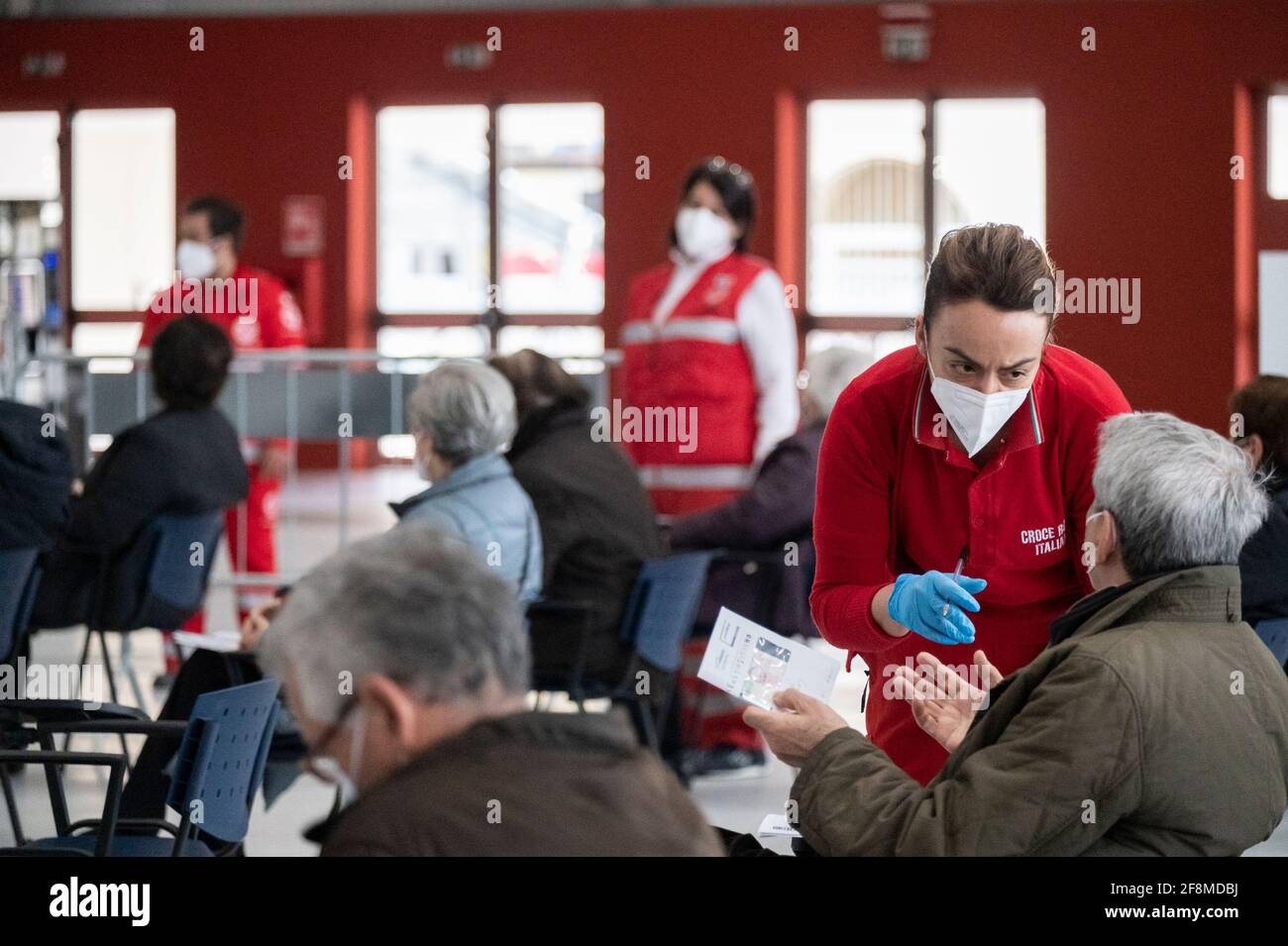 Un membro della Croce Rossa ha visto parlare con un anziano. Al nuovo centro vaccinazioni Covid-19 del Centro Fieristico (Ente Fiera) di Catanzaro Lido, quasi 500 persone di età pari o superiore ai 70 anni, senza particolari patologie, hanno riservato il loro posto per ricevere il vaccino AstraZeneca. I membri della Croce Rossa Italiana e della protezione civile aiutano gli operatori sanitari locali in materia amministrativa e sanitaria per attuare il programma di vaccinazione. Foto Stock