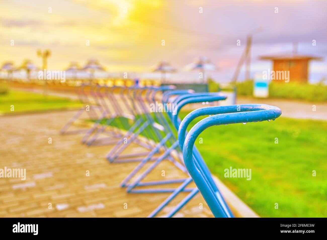 Posti di parcheggio per biciclette sull'oceano. Spiaggia di mare al tramonto. Ombrelloni e lettini in background. Prato verde e comodi sentieri per ciclisti. Vacanze weekend, vacanze estive. Foto Stock