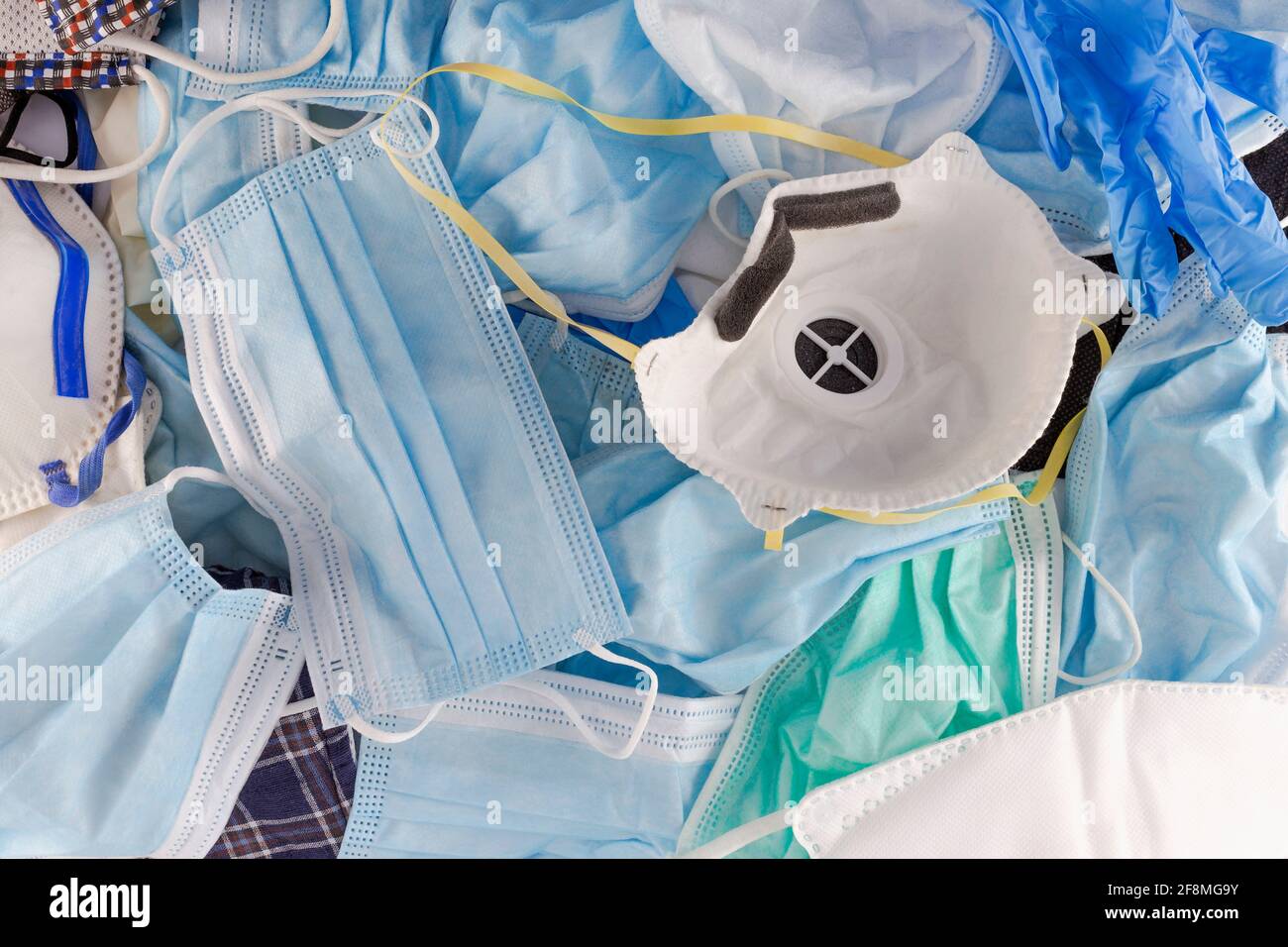 Un mucchio di maschere chirurgiche mediche con viso blu e respiratori monouso FFP2. Primo piano delle maschere facciali usate abbandonate molte impilate insieme. Pandemia B Foto Stock