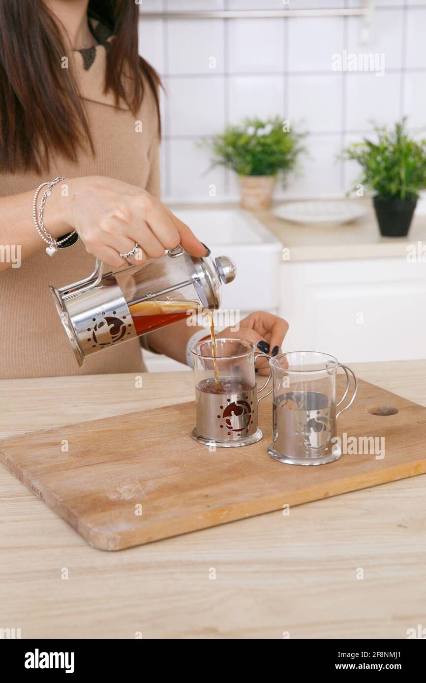 Una donna in una cucina scandinava leggera versa il tè una teiera in una tazza al mattino Foto Stock