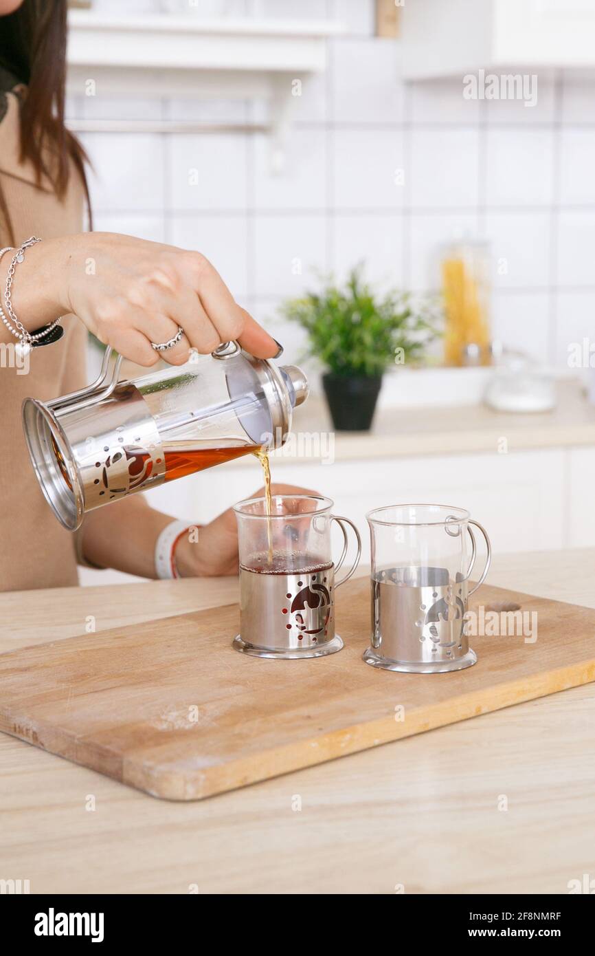 Una donna in una cucina scandinava leggera versa il tè una teiera in una tazza al mattino Foto Stock