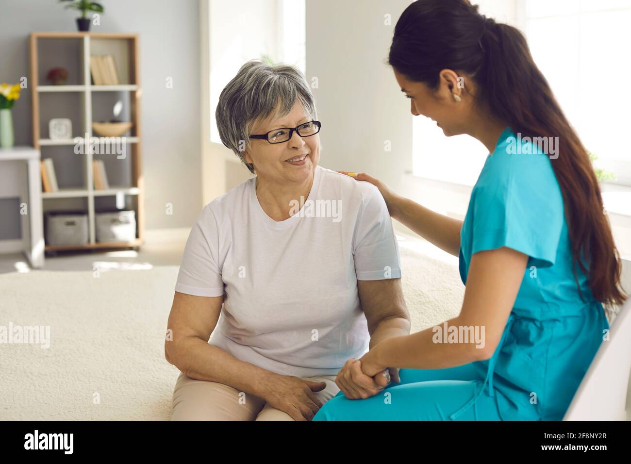 Un'infermiera cordiale e sorridente sostiene la paziente anziano seduto a casa divano Foto Stock