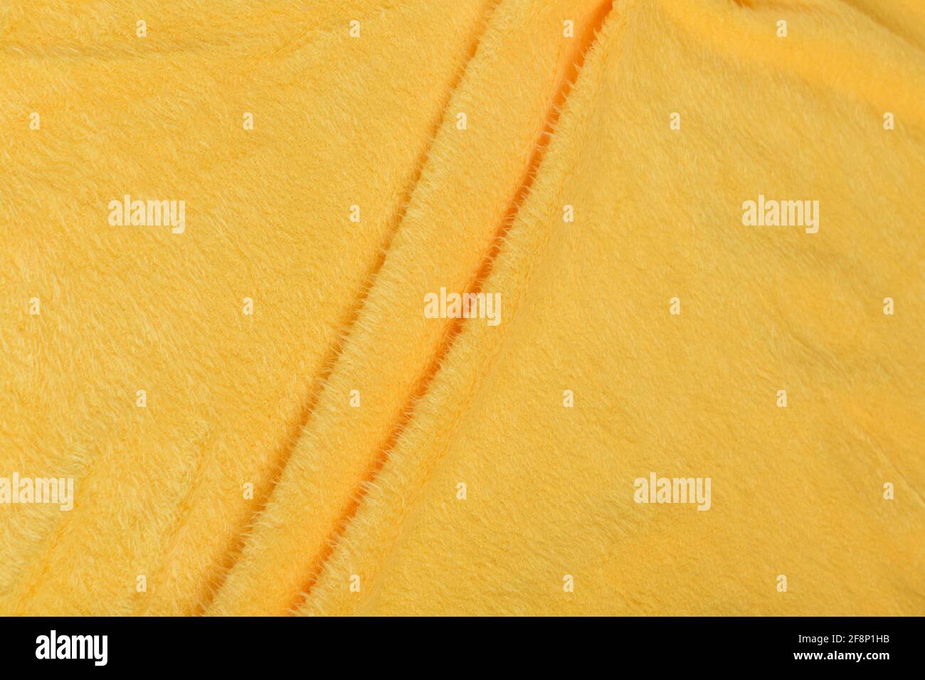 Tessuto satinato di colore giallo ripiegato a pieghe e onde con luci e texture che brillano nella luce Foto Stock