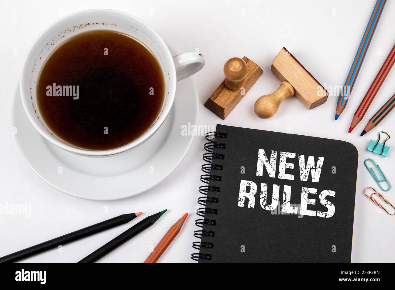 Nuove regole. Notebook nero, caffè e forniture per ufficio su un tavolo bianco. Foto Stock