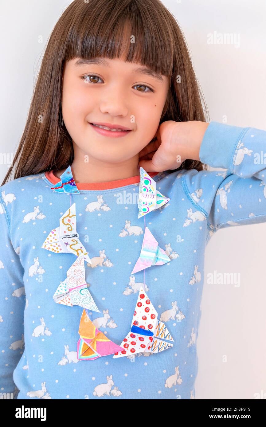 Ragazza di otto anni che indossa una collana origami Foto Stock
