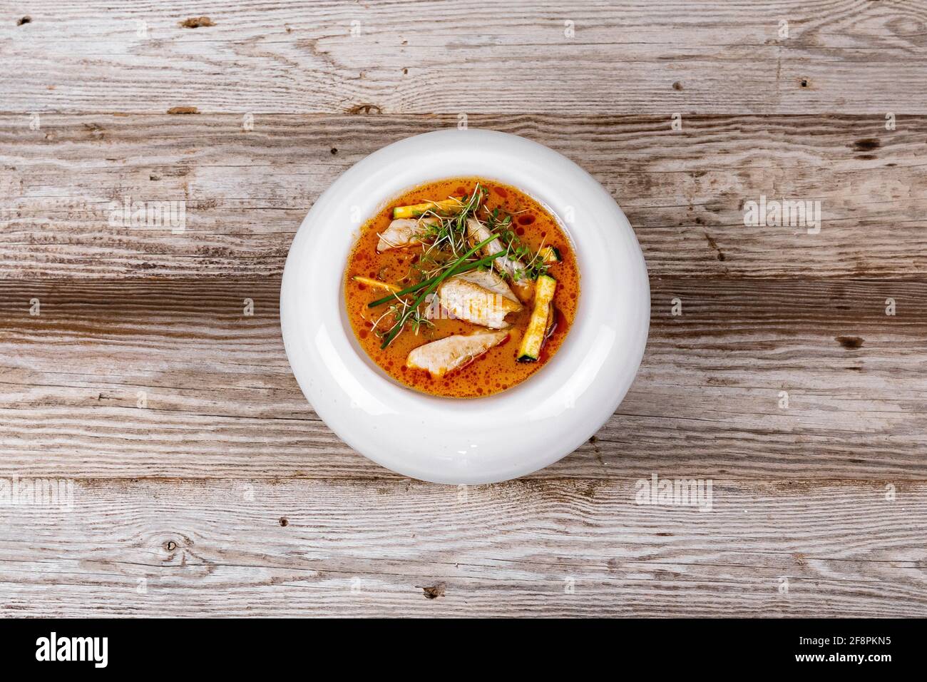 Zuppa Tom Yum con pollo su sfondo di legno in piatto bianco. Ingredienti brodo di pesce, spezie, latte di cocco, funghi, zucchine, Filetto di pollo Foto Stock