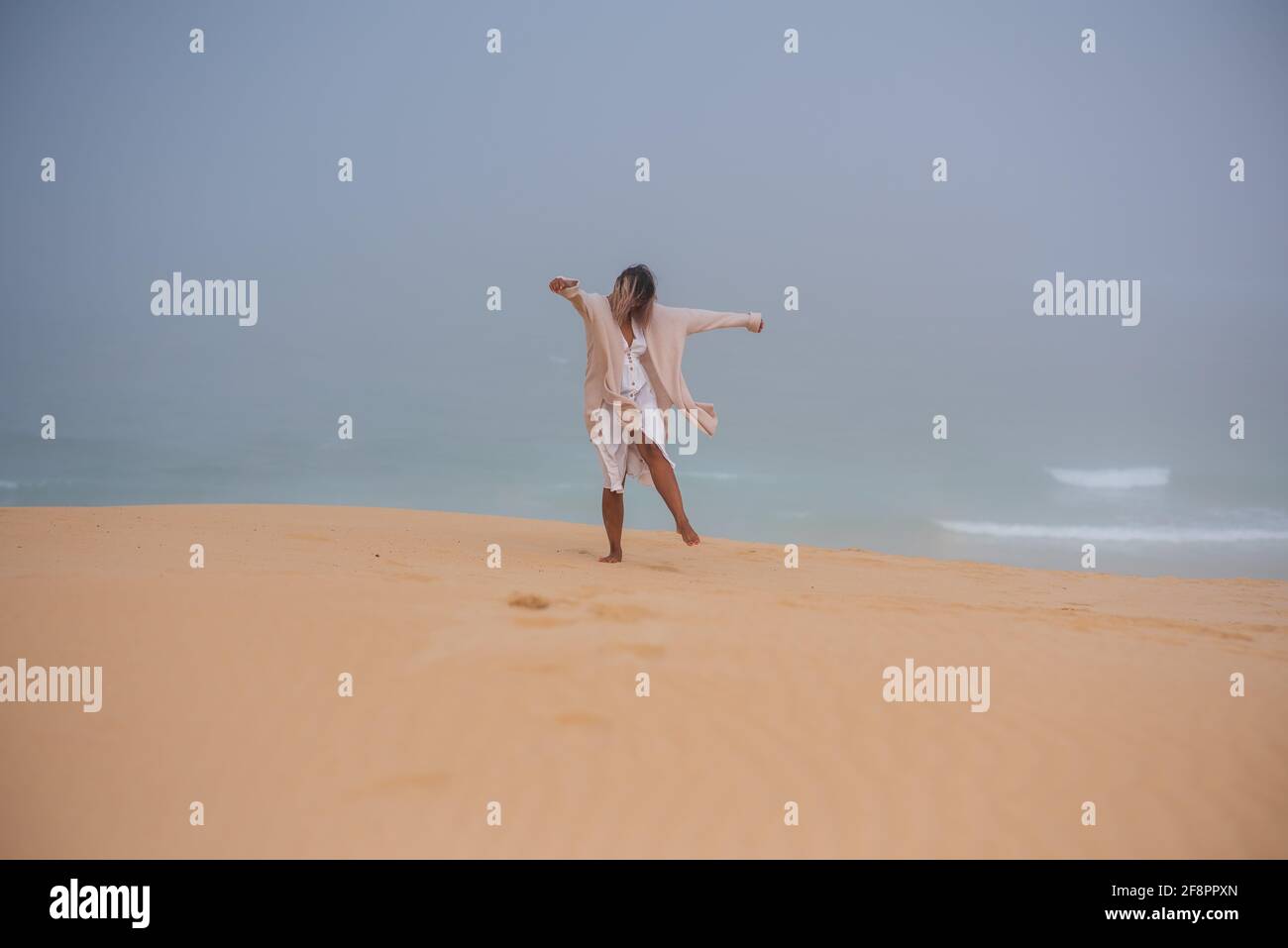 Donna che cammina da sole dune di sabbia con la spiaggia sullo sfondo Foto Stock