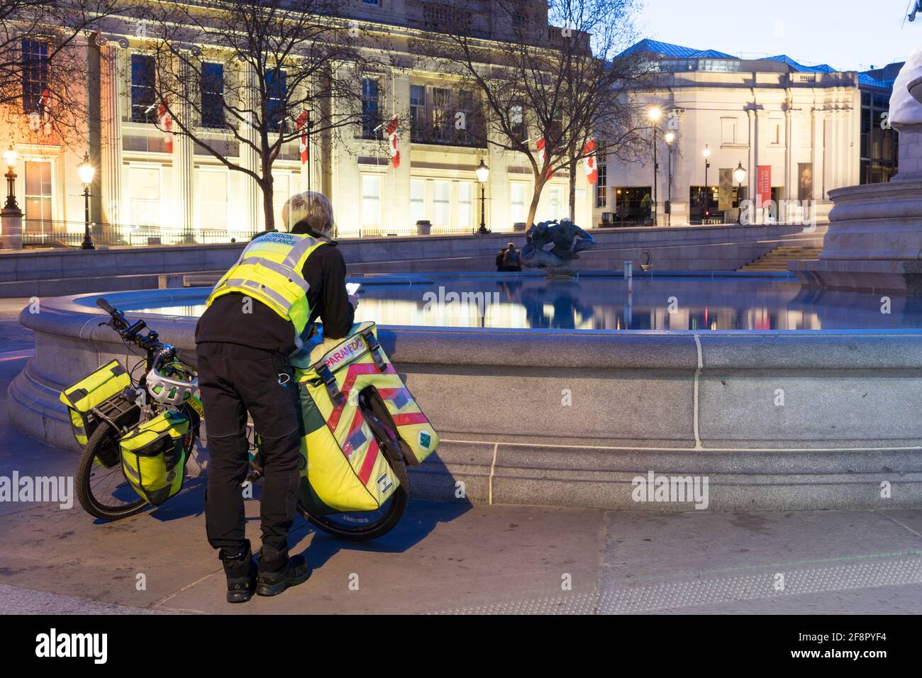 Un paramedico della bici dal servizio di ambulanza di Londra controlla il suo cellulare Per la prossima assegnazione accanto alla Fontana in piazza Trafalgar Foto Stock