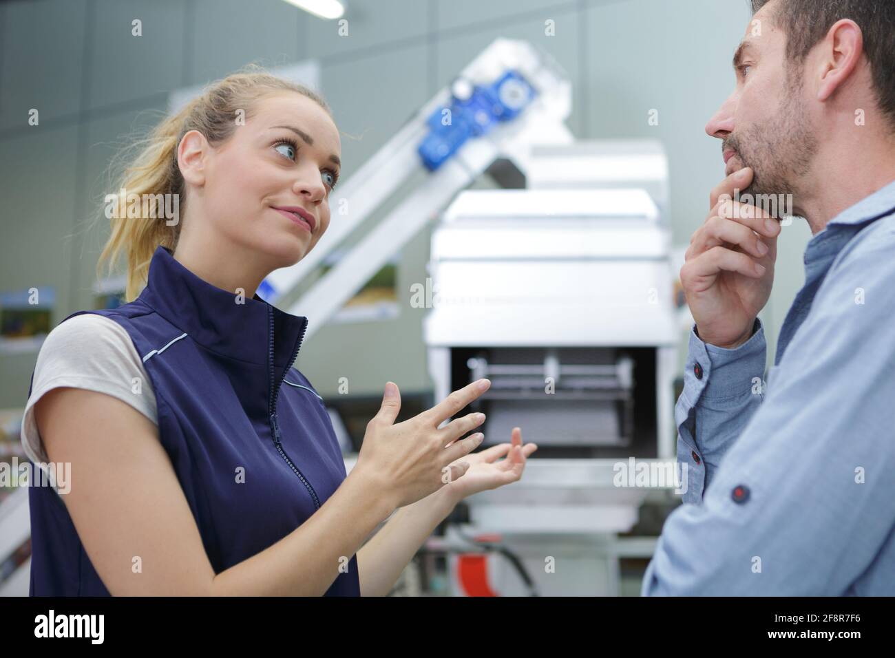 donna fabbrica operativa gesturing verso macchinari durante la discussione Foto Stock