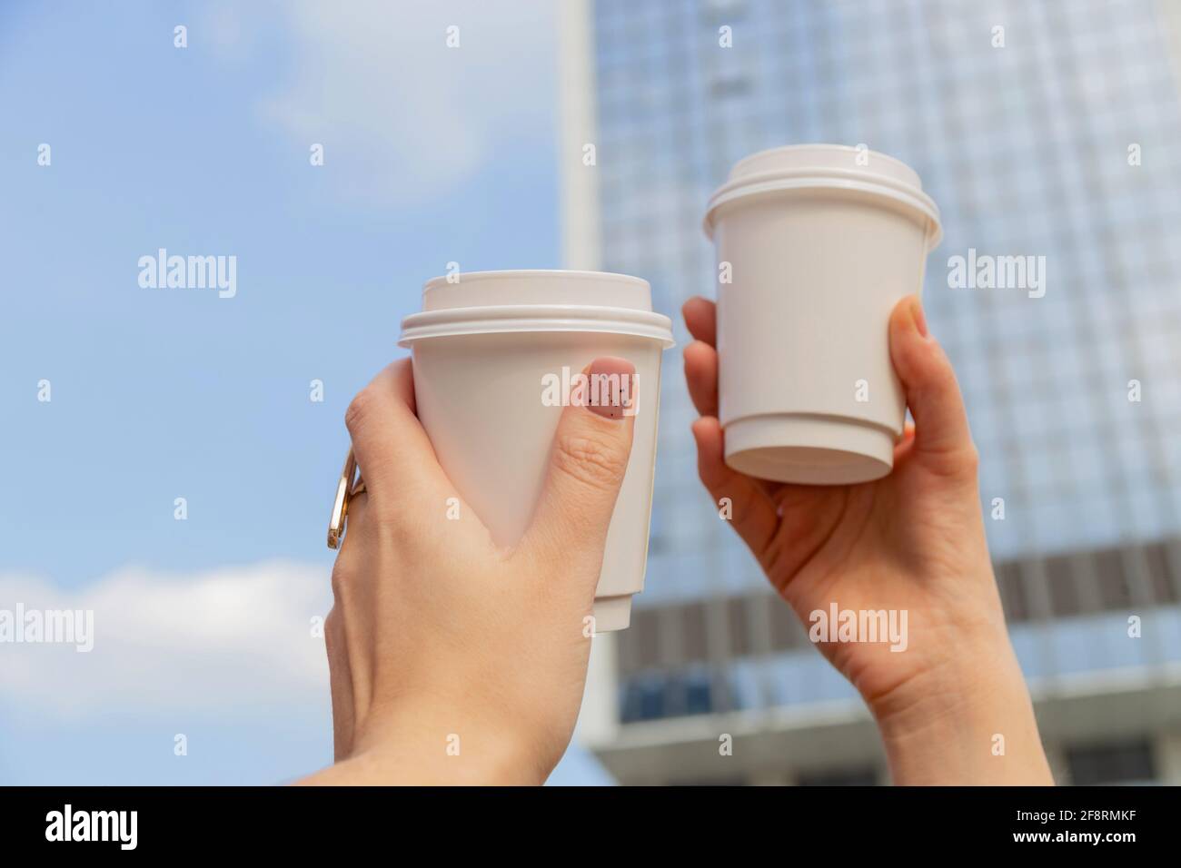 Due tazze bianche con caffè da utilizzare nelle mani femminili sullo sfondo degli edifici della città e del cielo Foto Stock