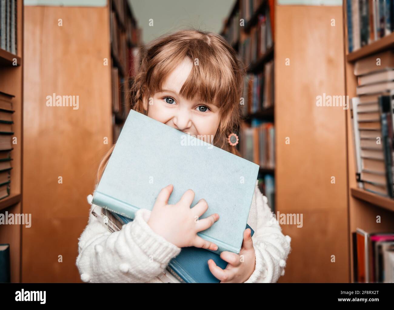 Bambina in biblioteca con libri in mano. Cute toddler esplora le librerie Foto Stock