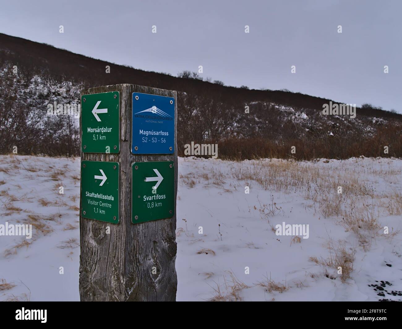 Cartello in legno accanto al sentiero escursionistico nel Parco Nazionale di Vatnajökull nella stagione invernale che mostra la direzione per la cascata Svartifoss con montagne innevate. Foto Stock