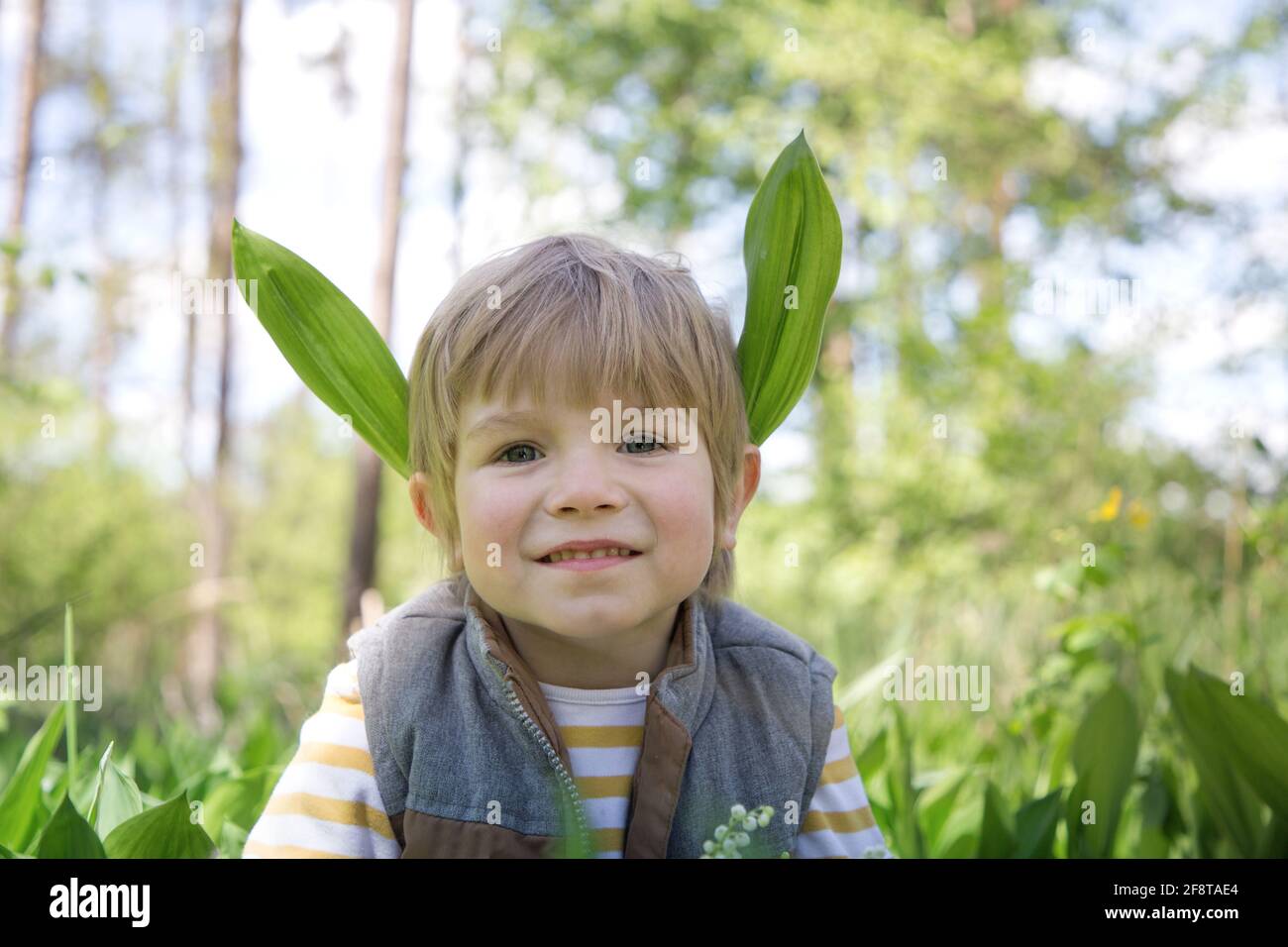 ragazzo carino di 4 anni in un giorno di primavera nella foresta. Dietro le  orecchie ha foglie di gigli della valle, assomiglia ad un elfo di legno.  Relax, playfu Foto stock - Alamy