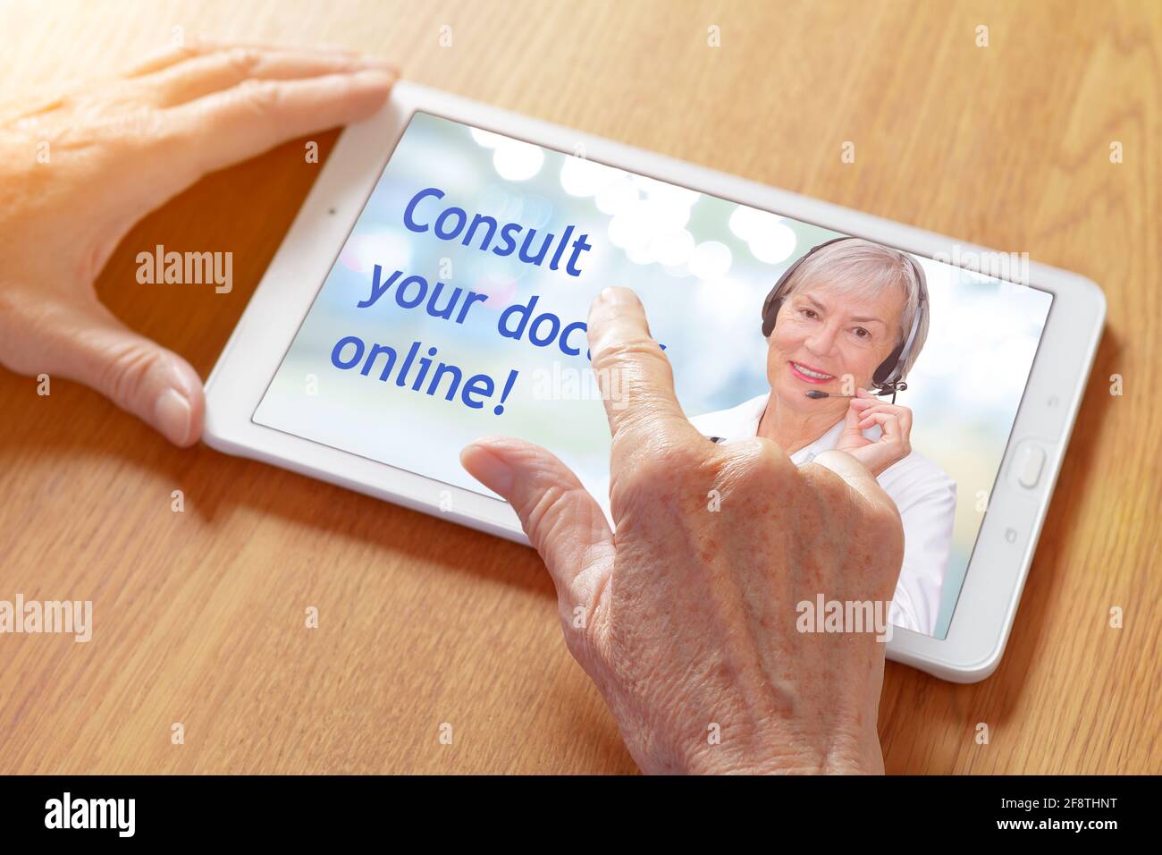 Mani che toccano un tablet pc con un'app di tele consulenze, mostrando un medico senior con l'auricolare e il testo: Consultare il medico online. Foto Stock