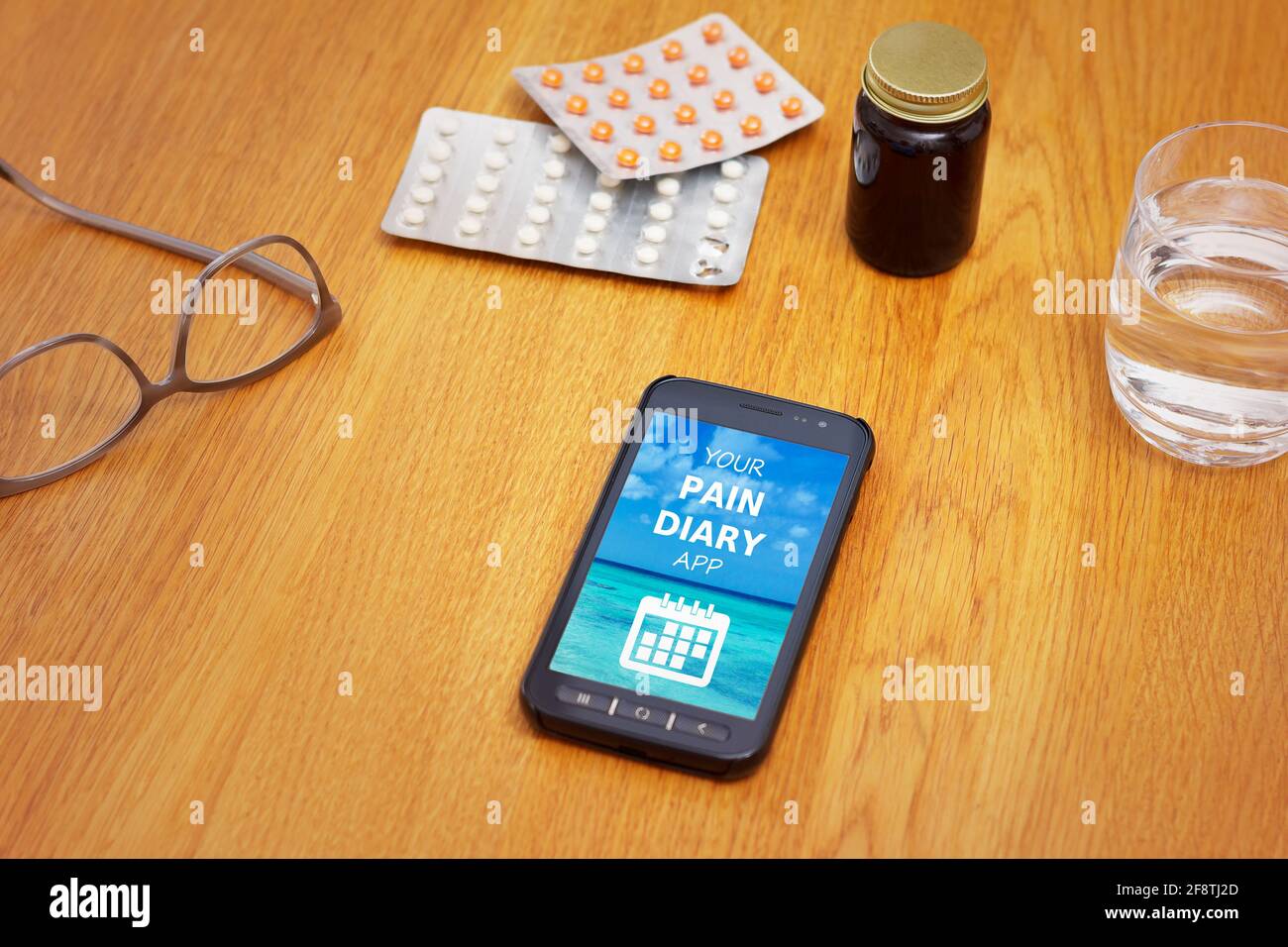 M-Health Concept: Un telefono cellulare che mostra un'applicazione mobile con il testo la tua app di agenda del dolore su un tavolo con medicina, bicchieri e acqua . Foto Stock