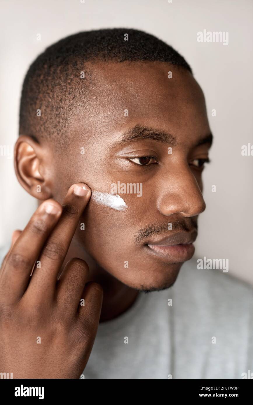 Giovane africano che applica crema idratante alla guancia Foto Stock